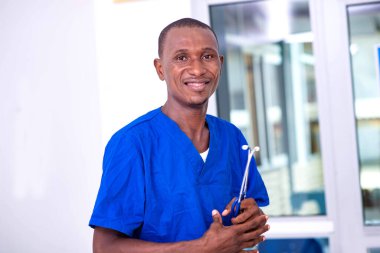 Genç adam mavi üniforma giyiyor ve kameraya gülümserken steteskop tutuyor..