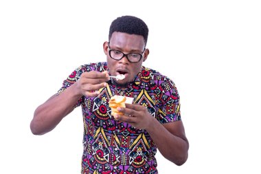 Beyaz arka planda duran gözlüklü yakışıklı genç bir işadamı süt eşliğinde kruvasan yiyor.