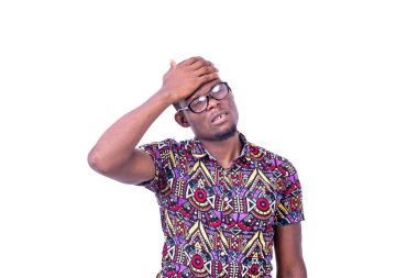 Beyaz arka planda duran gözlüklü genç bir adam elini alnına koyup baş ağrısından muzdarip.