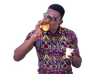 Beyaz arka planda duran gözlüklü yakışıklı genç bir işadamı kruvasan yiyor.