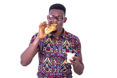 Yakışıklı genç adam kahvaltı yaparken kruvasan yiyor ve elinde süt tutuyor..