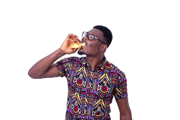 Beyaz arka planda duran gözlüklü yakışıklı genç bir işadamı kruvasan yiyor.