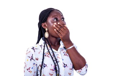 Uzun kollu bir gömlek giyen güzel bir kadın beyaz bir arka planda duruyor ve eli ağzını kapatıyor. Şaşırmış görünüyor..