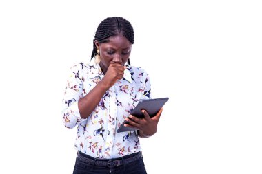 Gömlekli genç bir iş kadını izole edilmiş beyaz bir arka planda duruyor ve yumruğuyla ağzını kapayan tablete bakıyor..