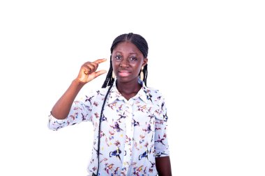 Beyaz arka planda duran örgülü genç bir kadın parmaklarıyla gülümseyerek küçük bir işaret yapıyor..