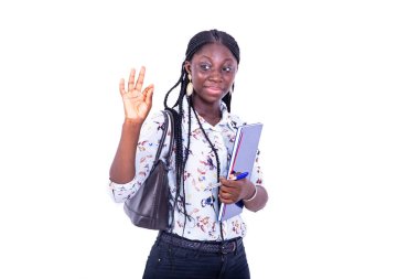Güzel genç kız öğrenci elinde defter tutuyor ve gülümserken parmaklarıyla iyi bir jest yapıyor..