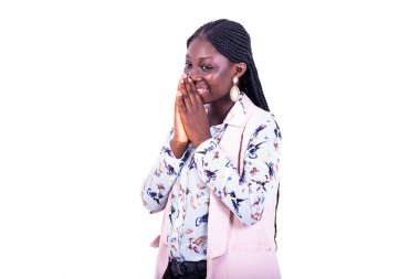 Ceketli genç ve güzel bir iş kadını beyaz arka planda duruyor ağzını kapatıyor ve gülümsüyor..