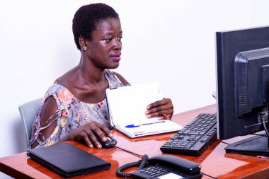 Ofiste dizüstü bilgisayarda çalışan genç ve ciddi bir iş kadını. Masasında açık bir defter var..