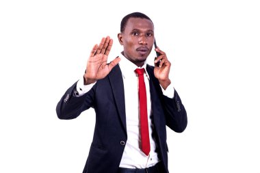 Beyaz arka planda duran ceketli yakışıklı bir işadamı cep telefonuyla el hareketi yapıyor..