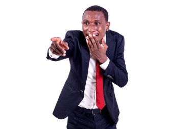 Beyaz arka planda dikilen takım elbiseli bir işadamı, eli dudaklarını kapatmış gülen bir parmağı işaret ediyor..