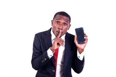 Beyaz arka planda duran ceketli bir işadamı cep telefonunu sunuyor ve sessiz bir jest yapıyor..