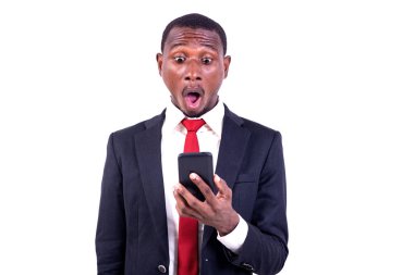 Beyaz arka planda duran bir işadamı şaşırmış bir şekilde cep telefonuna bakıyor..