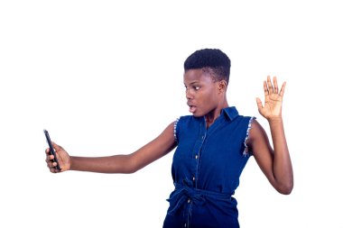 Güzel, şaşırmış genç bir kadının portresi cep telefonundaki bir video görüşmesi sırasında elini kaldırıyor..