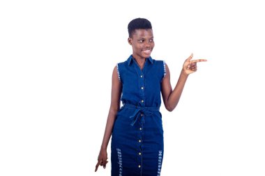 Kot pantolonlu genç bir kız beyaz arka planda durup parmağını göstererek gülümsüyor..