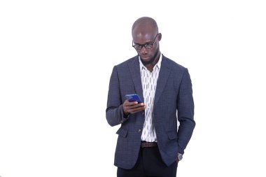 Beyaz arka planda duran ceketli genç bir işadamı cep telefonundan mesajlar okuyor..