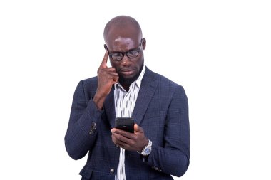 Beyaz arka planda duran ceketli genç bir işadamı cep telefonuna bakarken.