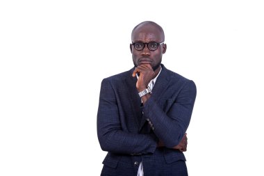 Beyaz arka planda duran ceketli genç bir işadamı. Elleri çenesinin altında kameraya bakıyor..