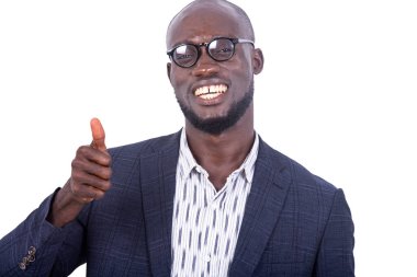 Beyaz arka planda duran gri takım elbiseli genç bir işadamı gülümserken iyi bir hareket gösteriyor..