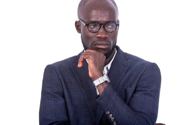 Gri takım elbiseli genç bir işadamı beyaz bir arka planda eli çenesinin altında ve hoşnutsuzlukla başka yere bakıyor..