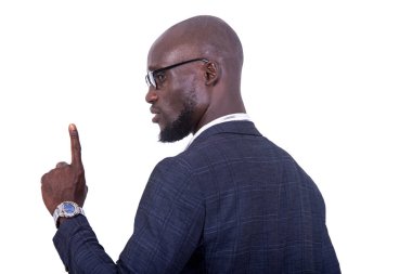 Beyaz arka planda duran gri takım elbiseli genç bir işadamı parmağını kameraya doğru kaldırıyor..