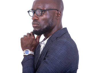 Gri takım elbiseli genç bir işadamı beyaz arka planda duruyor, elleri çenesinin altında ve profiline bakıyor..