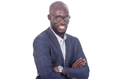 Gri takım elbiseli genç bir işadamı beyaz bir arka planda durup kollarını kavuşturup kameraya gülümsüyor..