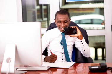 Ofisteki bilgisayarın önünde oturan işadamı bir belgeye gülümsüyor..