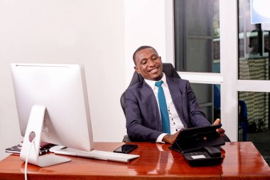 Takım elbiseli bir işadamı masada oturmuş tablet kullanarak gülümsüyor..