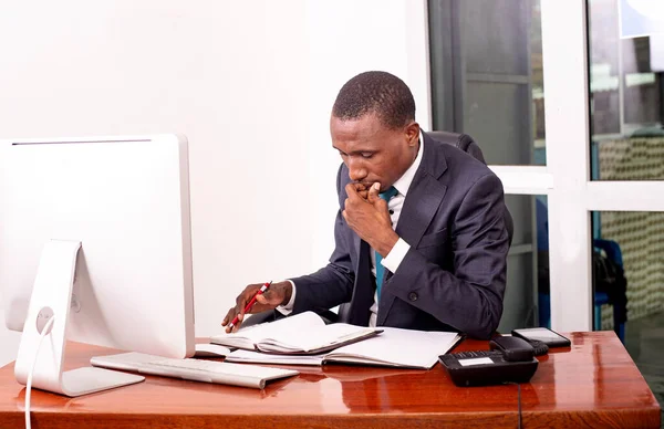 事務所のコンピュータの前に座って書類のメモを確認する重大なビジネスマン — ストック写真
