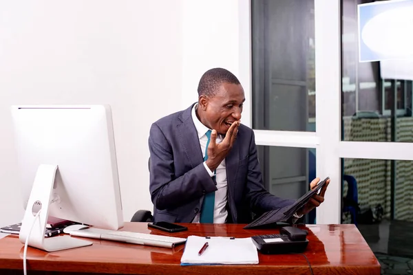 Takım elbiseli bir işadamı masada oturmuş tablete bakıyor. Şaşırmış bir şekilde bakıyor, gülümsüyor..