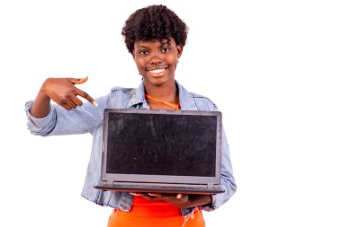 Beyaz arka planda duran ceketli genç bir öğrenci dizüstü bilgisayarını sunuyor ve gülümseyen kameraya bakıyor..