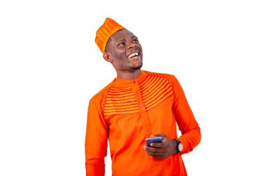 Beyaz arka planda duran turuncu elbiseli yakışıklı bir işadamı elinde cep telefonuyla yukarı bakıp gülüyor.