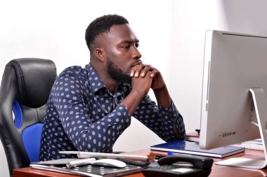 Ofisteki dizüstü bilgisayara bakarak ellerini çapraz yapmış genç bir iş adamının portresi..