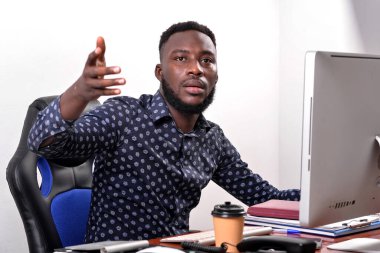 Genç bir iş adamının portresi. Ofisinde dizüstü bilgisayarın önünde oturuyor ve eliyle el kol hareketi yapıyor..