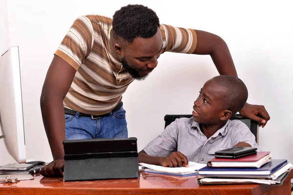 a young father in a t-shirt in an office guiding his child to do homework using a tablet while smiling.