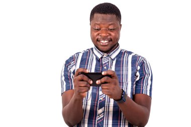 Kısa kollu gömlekli genç bir adam beyaz arka planda duruyor cep telefonuyla oyunlar oynuyor, gülümsüyor..