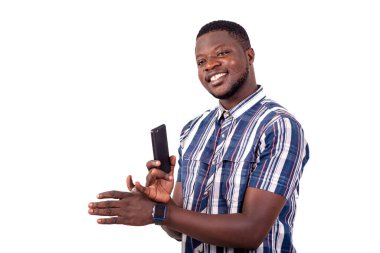 Kısa kollu gömlekli genç bir adam beyaz arka planda duruyor cep telefonunu tutuyor ve gülümseyen kameraya bakıyor..