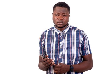 Beyaz arka planda duran gömlekli genç bir adam cep telefonunu tutarken.