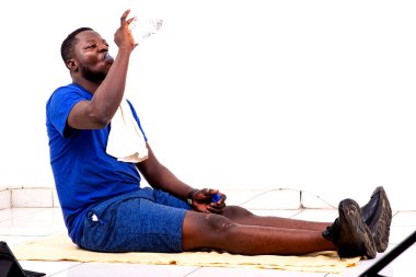 Spor kıyafetli yorgun bir gencin portresi. Plastik şişeden doğal su içerken oturuyor..