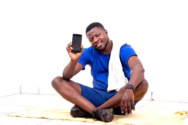 Yakışıklı bir genç adamın portresi yerde oturuyor ve gülümserken cep telefonunu gösteriyor..