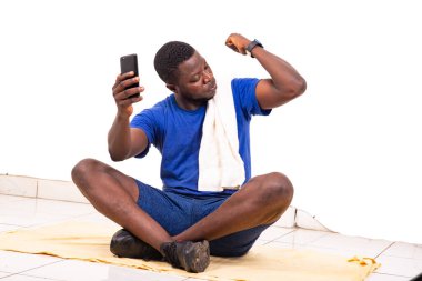 Yakışıklı bir genç adamın portresi yerde oturuyor ve pazılarını gösterirken cep telefonunu tutuyor..