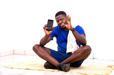 Yakışıklı, genç bir adamın portresi. Yerde oturmuş cep telefonunu gösteriyor ve gülümsüyor.