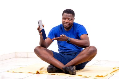 Spor kıyafetleri giymiş yakışıklı bir genç adamın portresi yere oturmuş elini dijital tabletin ekranına doğrultuyor ve gülümsüyor..