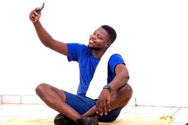 Yerde oturmuş gülümserken cep telefonuyla fotoğraf çeken yakışıklı bir gencin portresi..