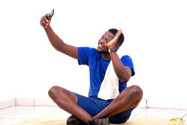 Yakışıklı, genç bir adamın portresi. Yerde oturuyor ve cep telefonundaki bir video görüşmesi sırasında elini sallıyor..