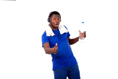 Boynunda havluyla, kulaklıkla plastik bir su şişesi tutan ve baş parmağını gösteren yakışıklı bir genç adamın portresi..