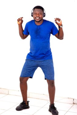 Boynunda havluyla spor salonunda durmuş kulaklıkla müzik dinliyor ve gülümsüyor..