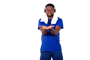 Spor kıyafetli genç bir adam spor salonunda duruyor kulaklıkları ve havlusu boynunda ve avuçlarında gülümsemesiyle..