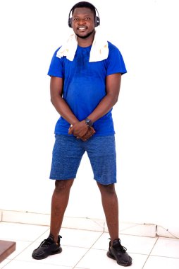 Boynunda havluyla bir odada dikilmiş müzik dinleyen, kulaklıkla spor yapan genç bir adam..