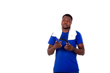 Spor kıyafetli genç bir adam spor salonunda durup kulaklık tutarken konuşuyor..